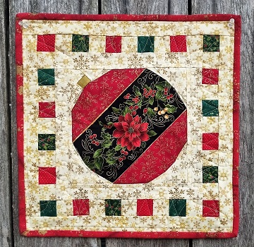 A decorative quilt featuring a large red ornament with a floral design in the center, surrounded by a border of alternating red, green, and white squares, all set against a golden background.